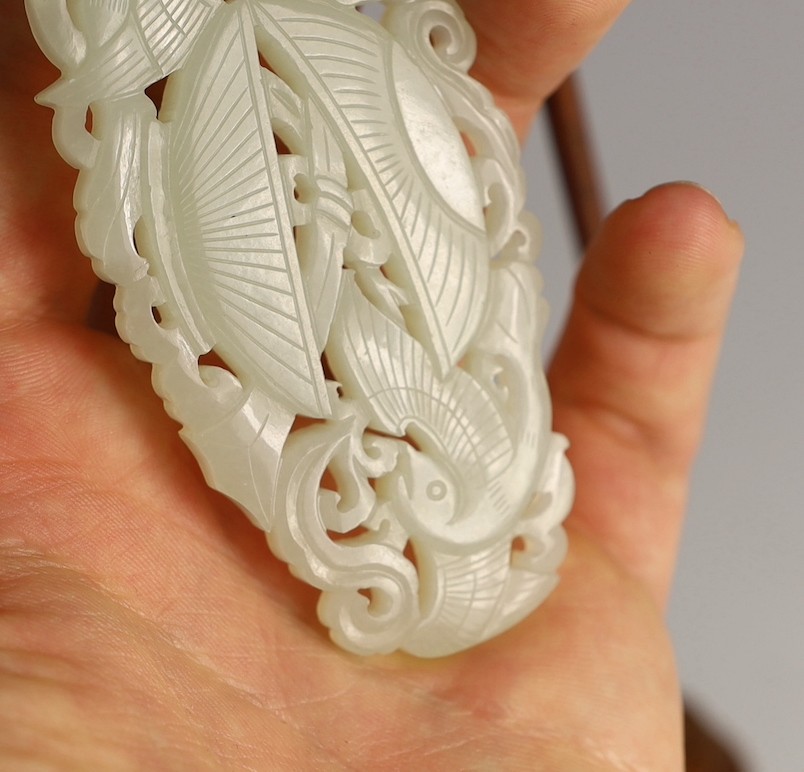 A Chinese white jade twin phoenix reticulated plaque, 19th century, 8.7cm, suspended from a wood stand with coral bead to the cord